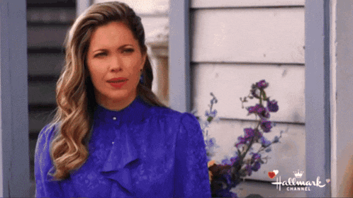 a woman in a purple top is standing in front of a house with purple flowers and the words hallmark channel on the bottom right