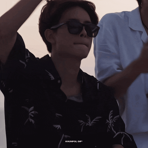 a man wearing sunglasses and a black shirt with palm trees on it has khunpol gif on the bottom right