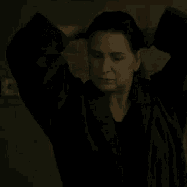 a woman in a black robe is standing in a dark room holding a hammer to her head .