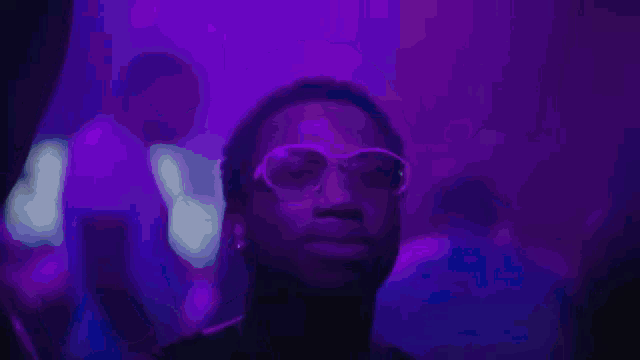 a man wearing sunglasses is standing in front of a purple light