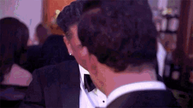 a man in a tuxedo is kissing another man