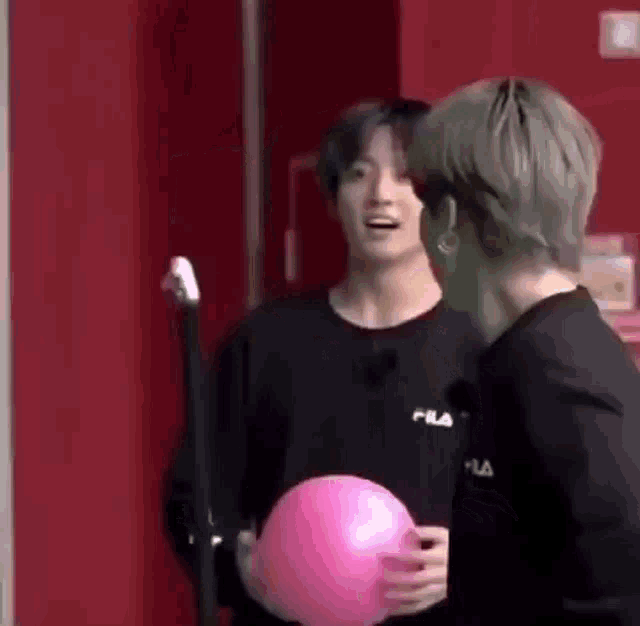 two men are standing next to each other and one is holding a pink ball .