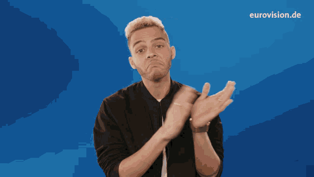 a man claps his hands in front of a blue background with eurovision.de written on it