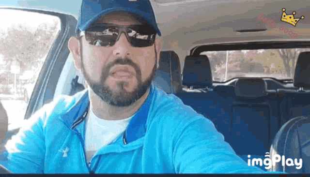 a man wearing sunglasses and a hat is sitting in a car with a baby king logo on the bottom right
