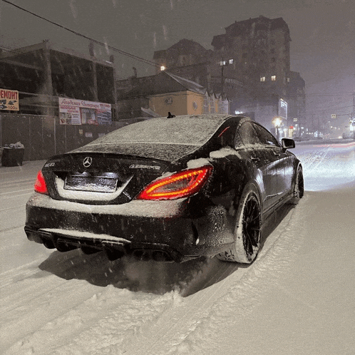 a black car is driving down a snowy street in front of a sign that says ремонт