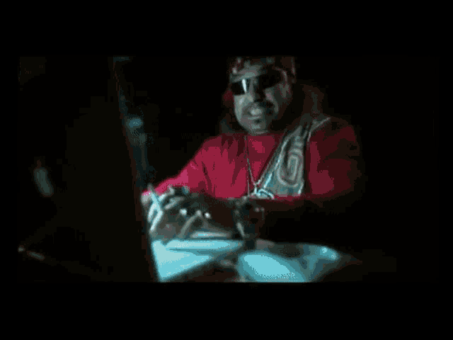 a man in a red shirt is sitting in front of a computer monitor