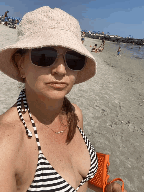 a woman wearing a bikini and a hat is standing on a beach