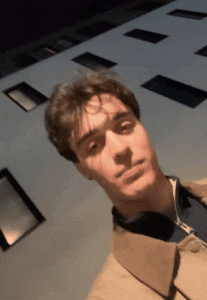 a young man wearing headphones looks at the camera with a building in the background