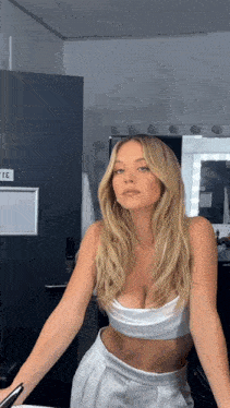 a woman in a white crop top and white pants is standing in front of a mirror in a dressing room .