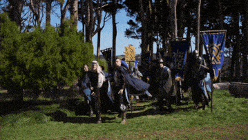 a group of men in armor are walking in a field with a blue banner that says ' knight ' on it