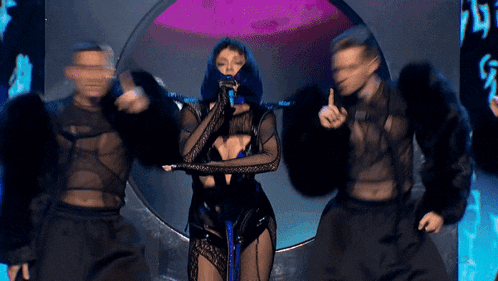 a woman is singing into a microphone while two men are dancing around her