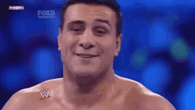 a man without a shirt is smiling in front of a blue background and has a w logo on his chest .
