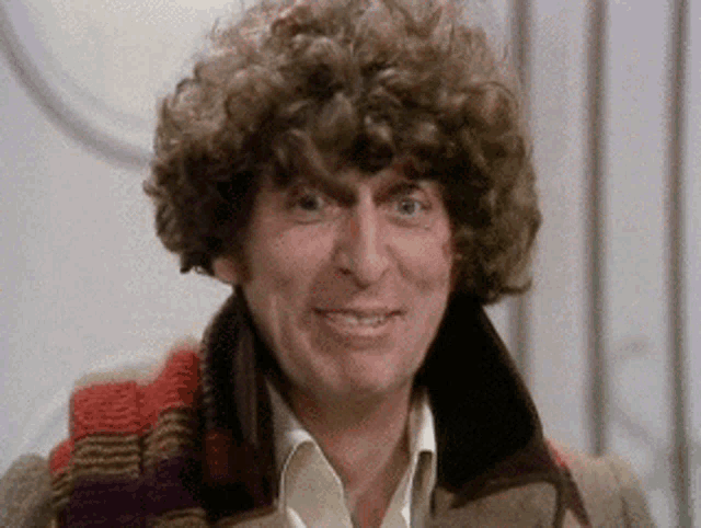 a close up of a man with curly hair wearing a scarf and a jacket .