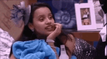 a woman is sitting on a bed with a blue blanket on her lap and talking on a cell phone .
