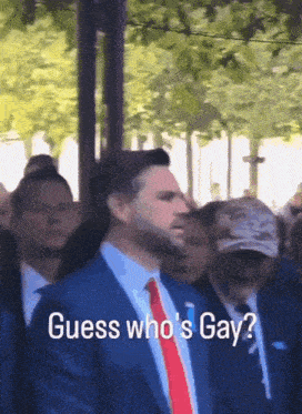 a man in a blue suit and red tie is standing in a crowd and says guess who 's gay