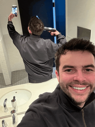 a man taking a picture of himself with a gun in front of a bathroom mirror
