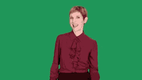 a woman in a red ruffled blouse is standing in front of a green screen and smiling .