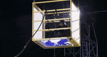 a man in a cage hanging from a rope with a blue background