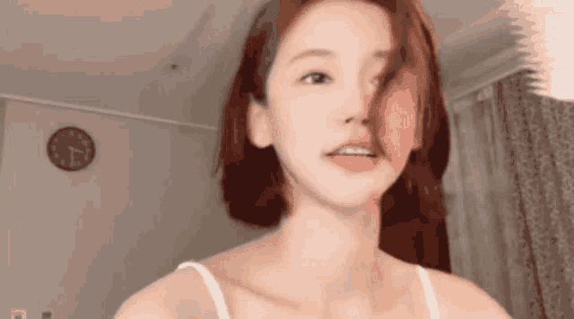 a woman in a white tank top is standing in a room with a clock in the background .