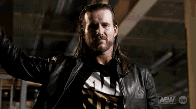 a man with long hair and a beard is wearing a black leather jacket that says aew