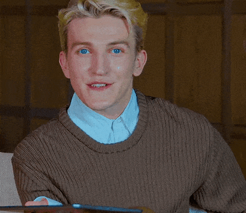 a man wearing a brown sweater is holding a tablet and smiling