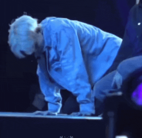 a man in a blue shirt is kneeling down on a stage with his head down .