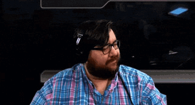 a man with a beard wearing headphones and a plaid shirt waves his hand