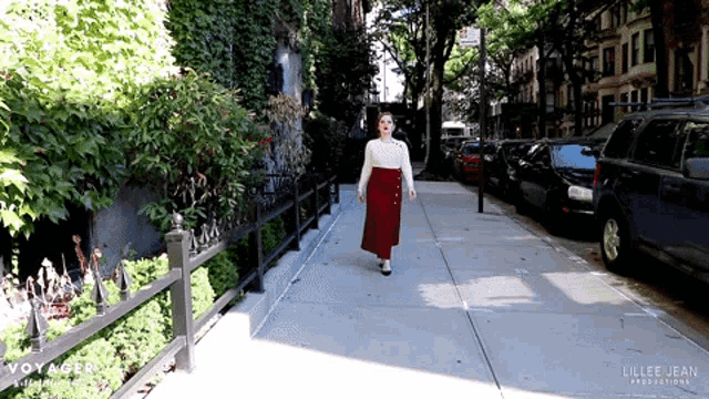 a woman in a red skirt walks down a sidewalk in front of a sign that says " voyager "