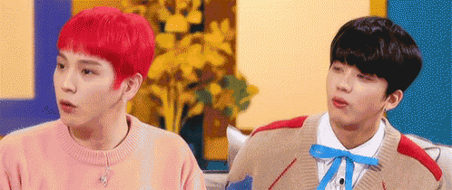 two young men are sitting next to each other on a couch . one of the men has red hair and the other has black hair .