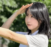 a young woman is covering her face with her hand while standing in front of trees .