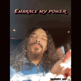 a man with curly hair and a beard is sitting in a car with the words " embrace my power " above him