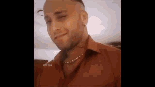 a bald man with a beard wearing a red shirt and a gold chain around his neck is smiling .