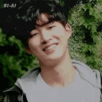 a young man with curly hair is smiling for the camera while standing in front of a tree .