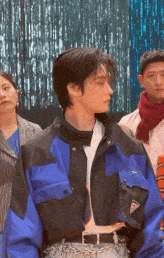 a man in a blue and black jacket is standing in front of a group of people in a room .