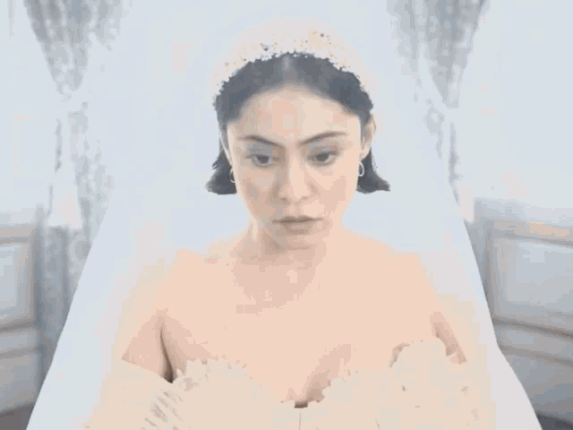 a woman in a wedding dress with a veil on looks at the camera
