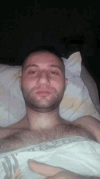 a man with a beard is laying on a bed with a blanket that says ' l ' on it