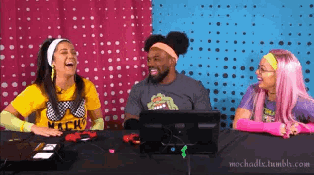 two women and a man are laughing in front of a screen with the website mochadix.tumblr.com in the lower right corner