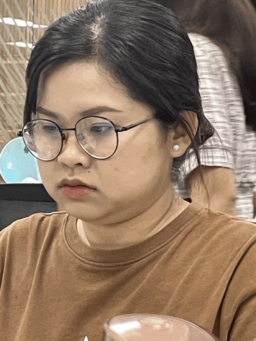 a woman wearing glasses and a brown shirt looks serious