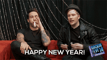 two men are sitting on a red couch and one of them is smoking a cigarette and the other is saying happy new year
