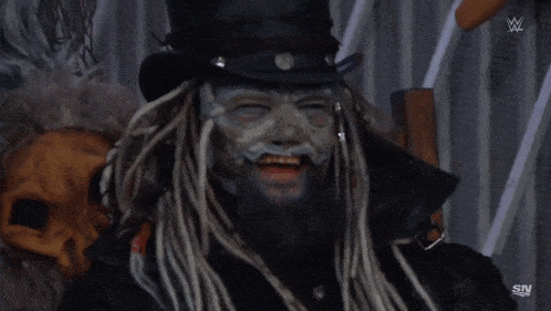 a man with dreadlocks and a top hat is sitting in front of a fence with sn written on it