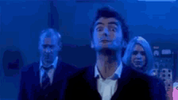 a man in a suit and tie is standing in a dark room with other people .