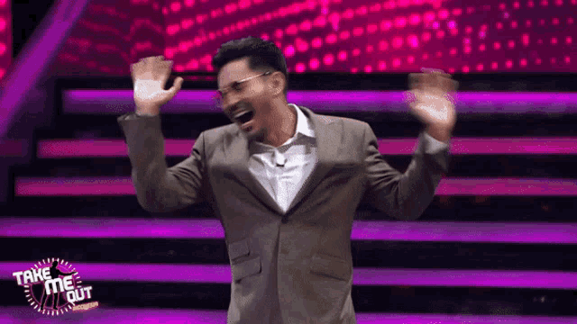 a man in a suit and glasses is standing on a stage with his arms in the air and the words take me out behind him