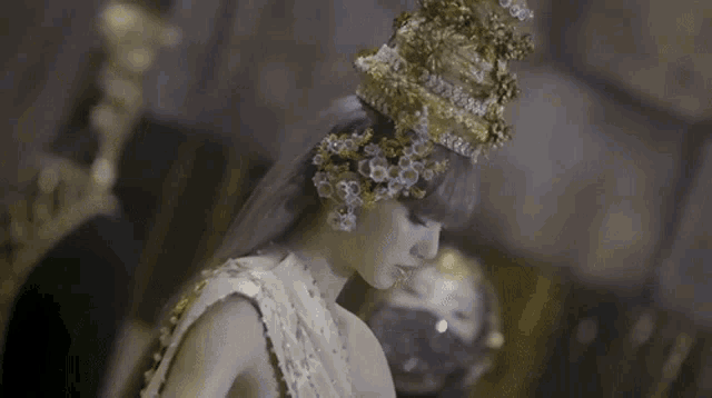 a woman wearing a white dress and a gold crown is standing in a dark room .