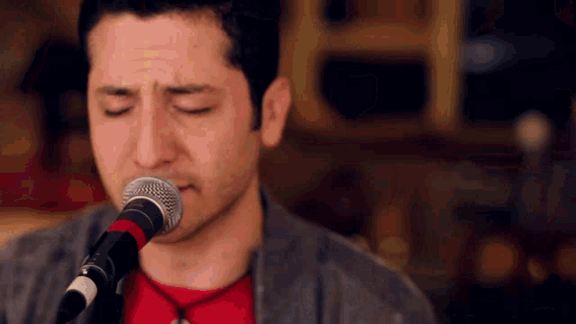 a man singing into a microphone with his eyes closed and a red shirt on