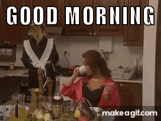 a woman is drinking a cup of coffee in a kitchen while a maid stands in the background .
