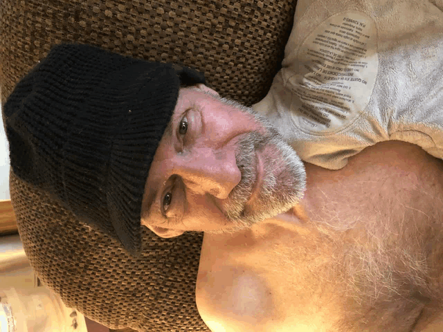 a man wearing a black hat is laying on a couch with a label on his shirt that says " no outerwear "