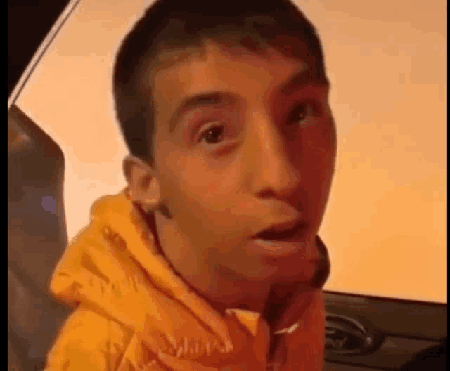 a young man wearing a yellow hoodie is making a funny face while sitting in a car .