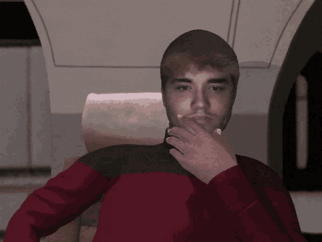 a man in a red and black shirt covering his nose