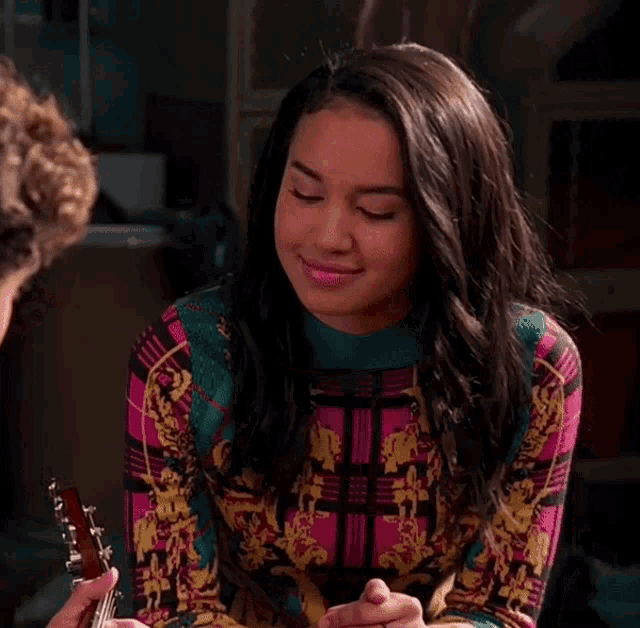a woman is smiling while sitting next to a man who is playing a guitar .
