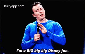 a man in a blue sweater is holding a microphone and saying `` i 'm a big big big disney fan ''